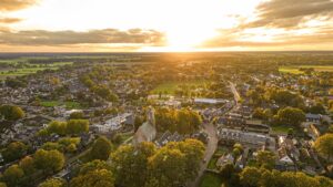 Luchtfoto van een dorp met maatschappelijk vastgoed zoals een kerk en andere publieke gebouwen, omgeven door groen, passend bij verduurzaming van maatschappelijk vastgoed.